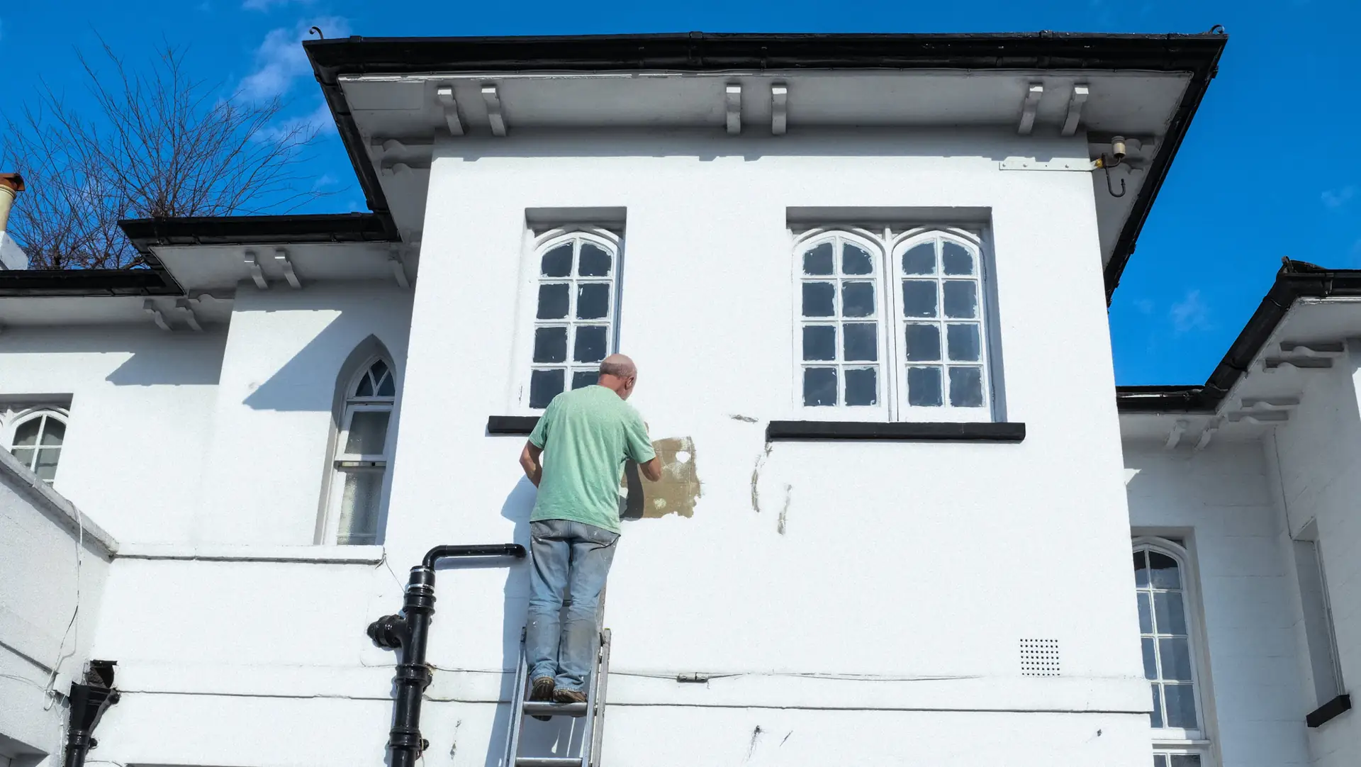 A painter on a ladder working on a white rendered house