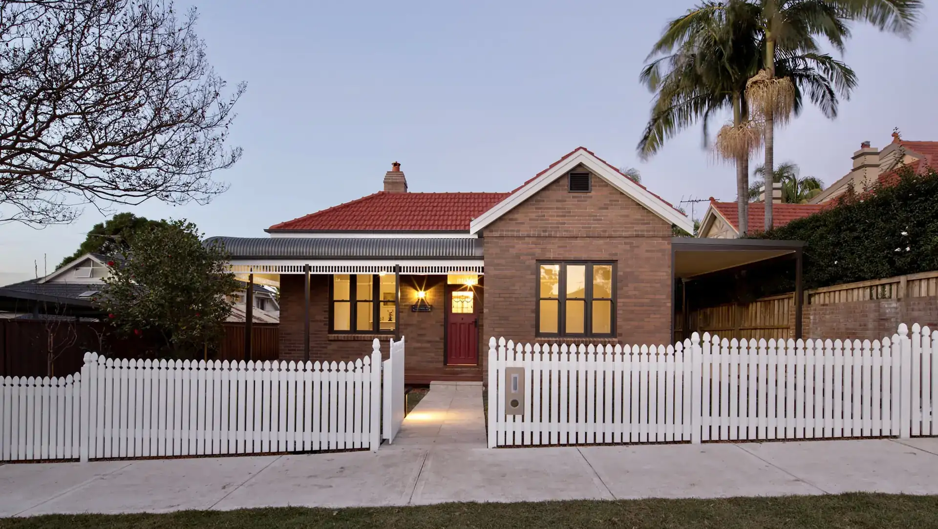 A brick home with a white picket fence at dusk